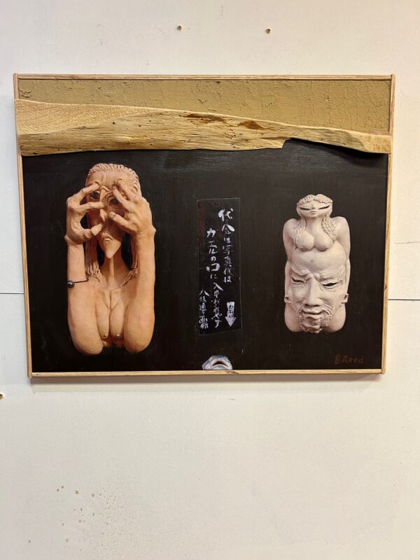 Framed artwork with two sculpted masks and calligraphy
